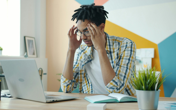 Man sits at desk massaging temples as he feels taken advantage of at work.