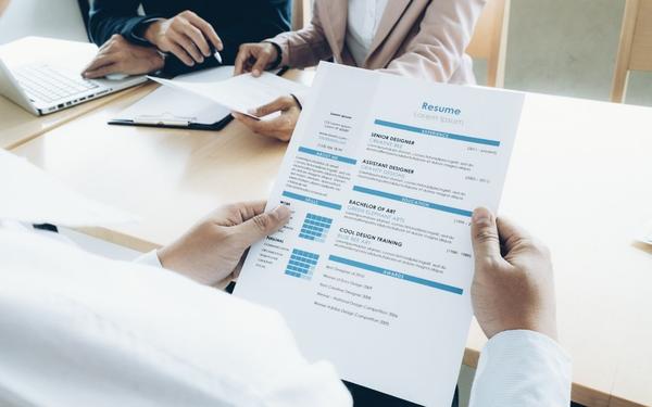A person holds a professional resume highlighting job titles like Senior Designer, representing the use of accurate, ATS-friendly job titles that support job search success.