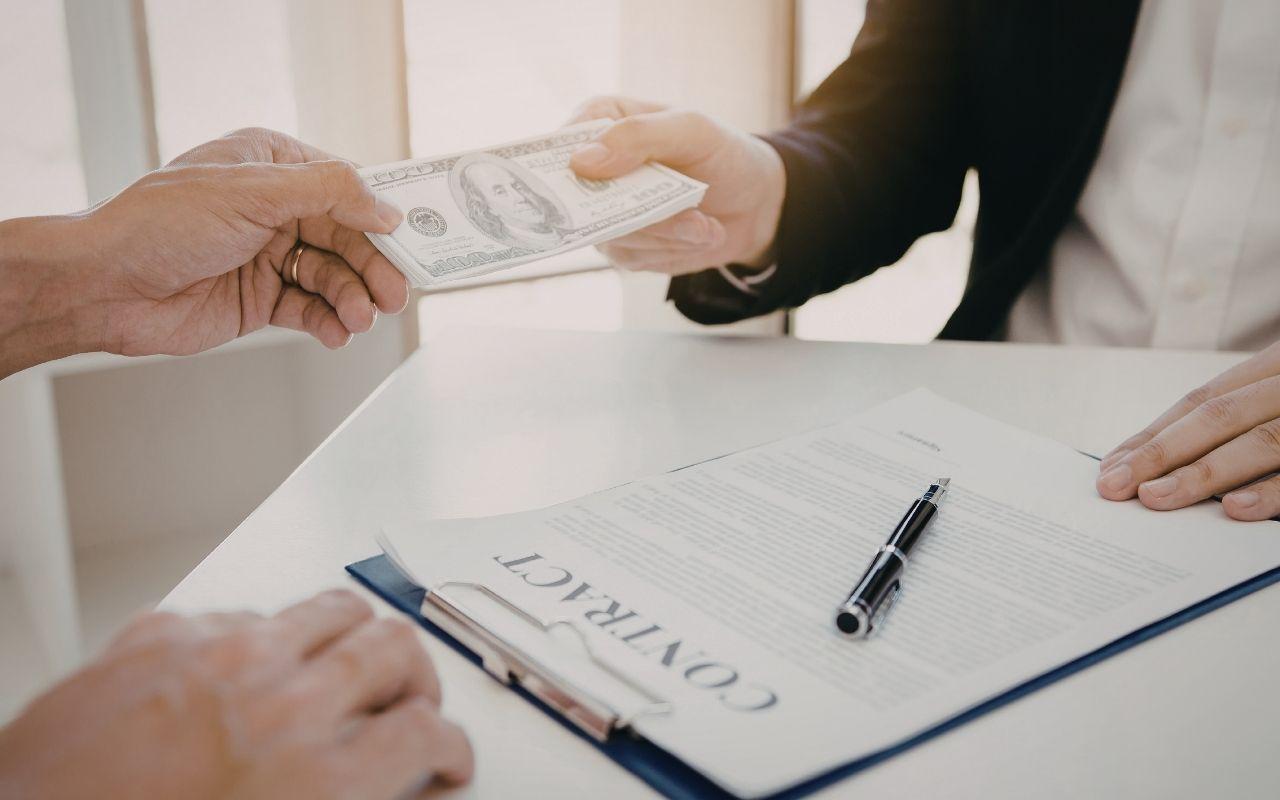 Two hands passing cash over a contract and pen, representing a salary negotiation for a new job offer.