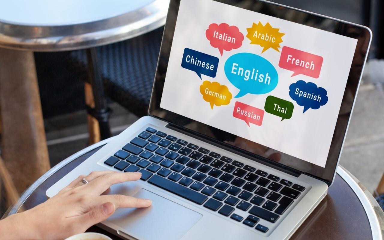 A laptop screen displaying colorful speech bubbles with "Hello" in various languages, representing multilingual skills to include on a resume.