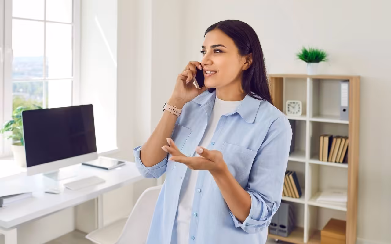 Person on a phone call in their home office, carefully declining a previously accepted job offer with a polite, professional expression.