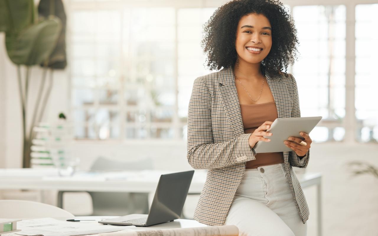 Confident female professional holding a tablet and smiling in a bright, sunlit modern corporate office space.