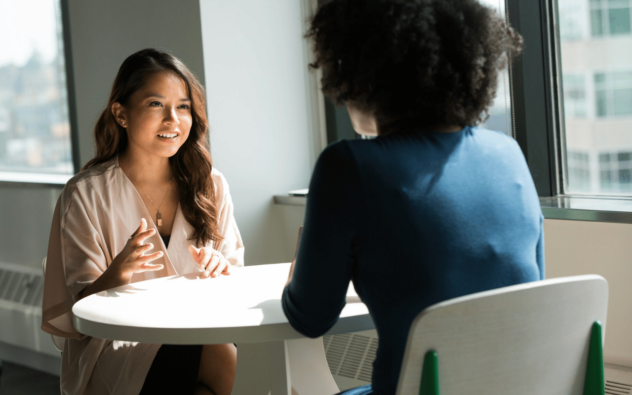 Professional woman speaking and gesturing during a one-on-one career mentoring session at table with colleague.