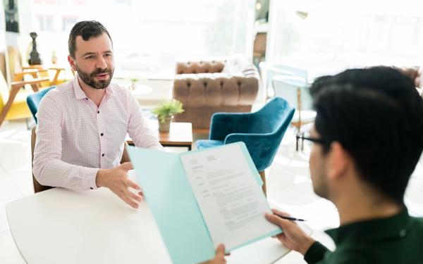 A job candidate gestures as he explains his resume work history and employment gaps to an interviewer.