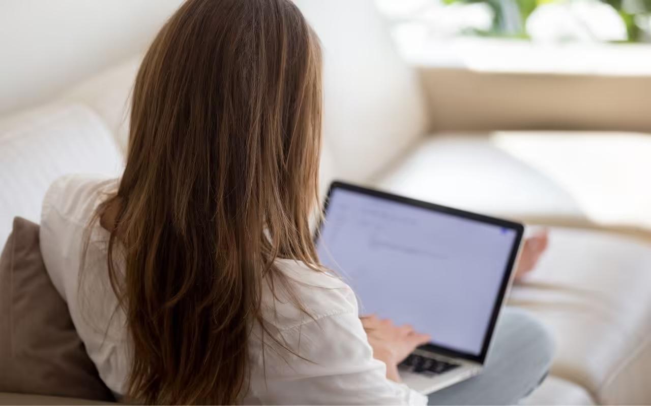 Woman sitting on a couch typing a professional letter of intent for a job application on her laptop.