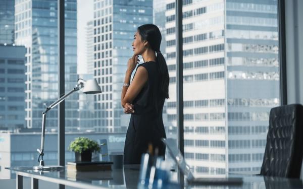 Confident professional in a sleek high-rise office, looking out a window at a city skyline, signaling success at a high-paying job.