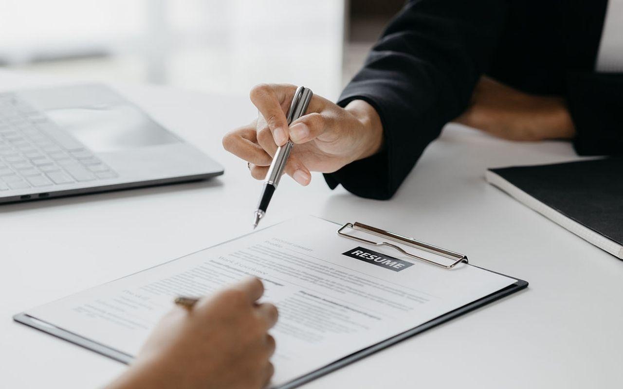 Close-up of two people reviewing a printed resume at a desk, pointing to a specific line on the page, illustrating the importance of using strong action verbs to make a resume stand out.