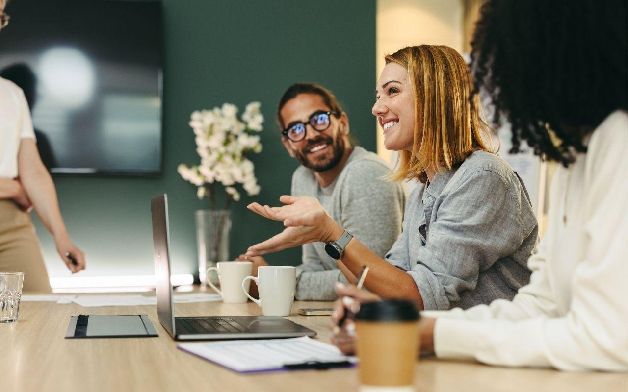 Coworkers in a meeting, with one person speaking and smiling while others smile and listen attentively, illustrating key soft skills like strong communication and teamwork.