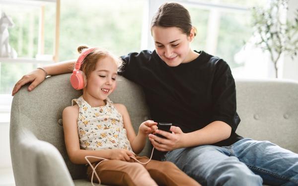 A teen working as a babysitter, helping a young girl select music on a phone during a classic high school job.