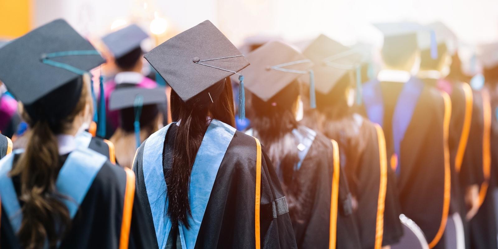 Graduates in caps and gowns stand in line at a commencement ceremony, representing new grads prioritizing job security over pay.
