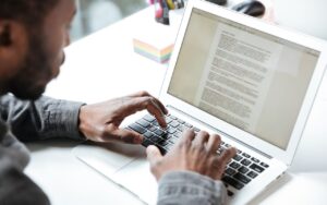 Person typing on a laptop at a desk, with the screen displaying a text document, representing writing or editing a cover letter.