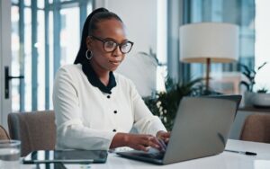 A woman in a modern office focuses intently as she types on a laptop, crafting a cover letter for internal positions or promotions.