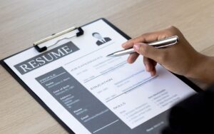 A close-up of a hand holding a pen over a professional resume on a clipboard, highlighting the job experience section.