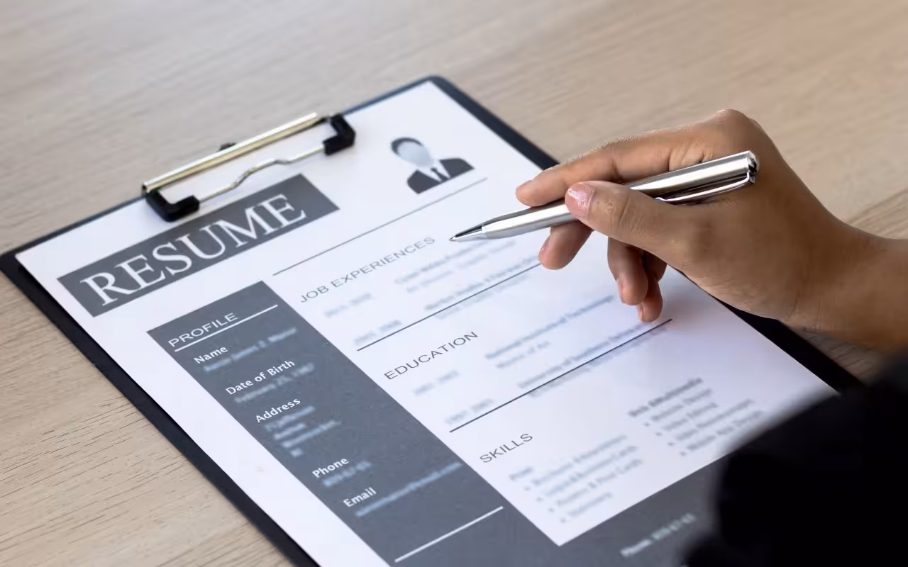 A close-up of a hand holding a pen over a professional resume on a clipboard, highlighting the job experience section.