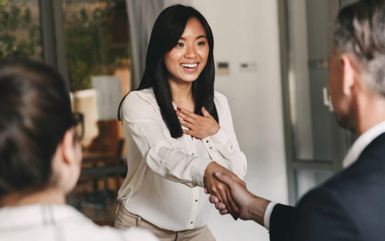 Smiling job candidate shaking hands with an interviewer during a successful job interview, representing fast hiring.