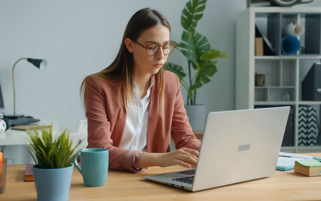 A hyper-focused young woman looks intently at her laptop screen while rapidly typing at a desk, illustrating a job seeker managing a high volume of applications.