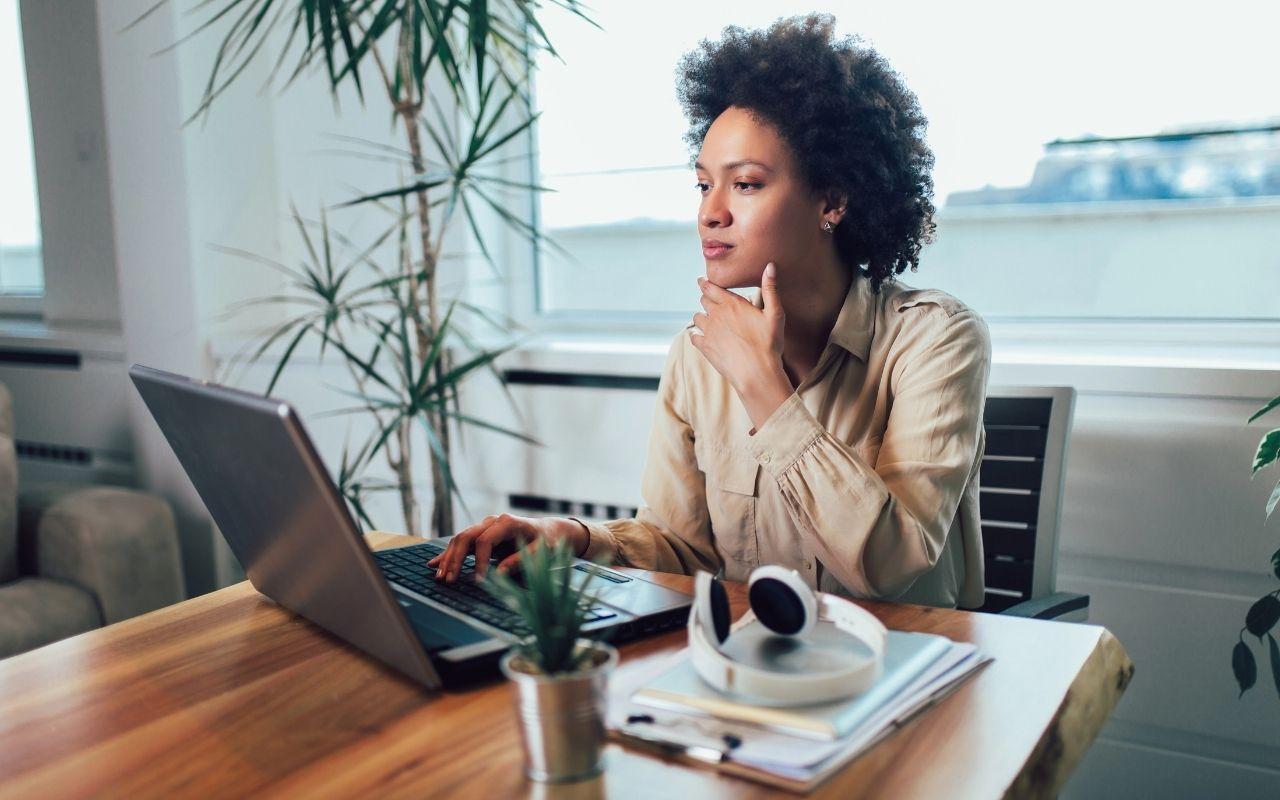 A job seeker thoughtfully evaluates a job posting on her laptop in a bright, modern office, seeking clarity.
